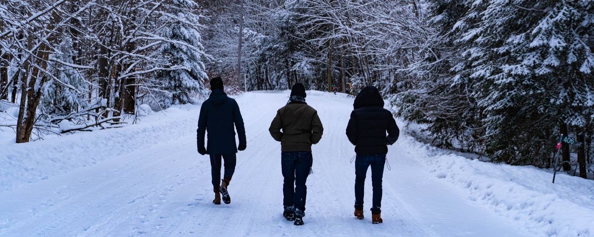 picture of three men walking on snow on a trail in a forest