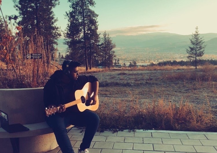 a picture of Mahir Rahman holding a guitar on a bench